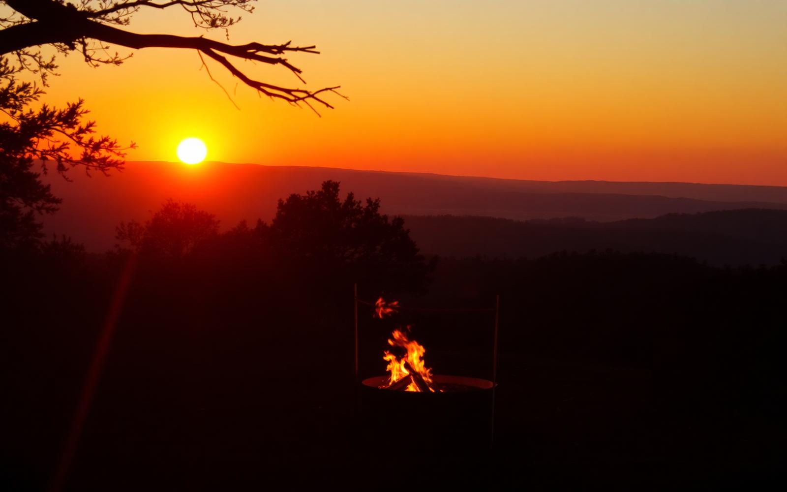 Entardecer alaranjado sobre a mata, com uma pequena fogueira acesa